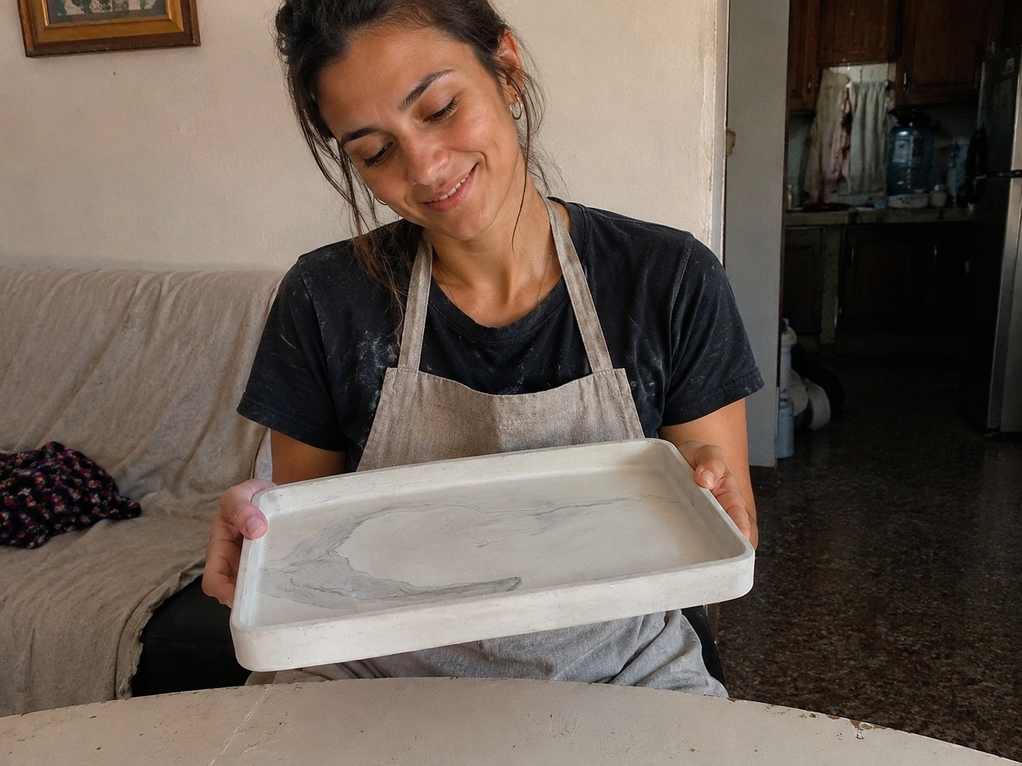 Mujer mostrando una bandeja decorativa de cemento terminada sobre una mesa con decoración minimalista